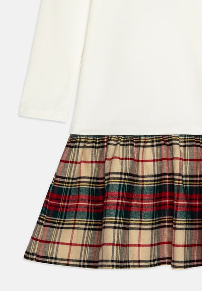 Dlhý rukáv top z krémovej látky spárovaný s károvanou sukňou s červenými, zelenými a čiernymi pruhmi na béžovom pozadí, navrhnutou s záhybmi.