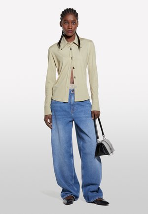 Chemise beige à manches longues, associée à un jean large bleu clair. Les accessoires comprennent un petit sac à main noir et des chaussures pointues.