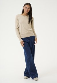Beige knit sweater with long sleeves and a round neckline, paired with wide-leg dark blue denim jeans and light-colored shoes.