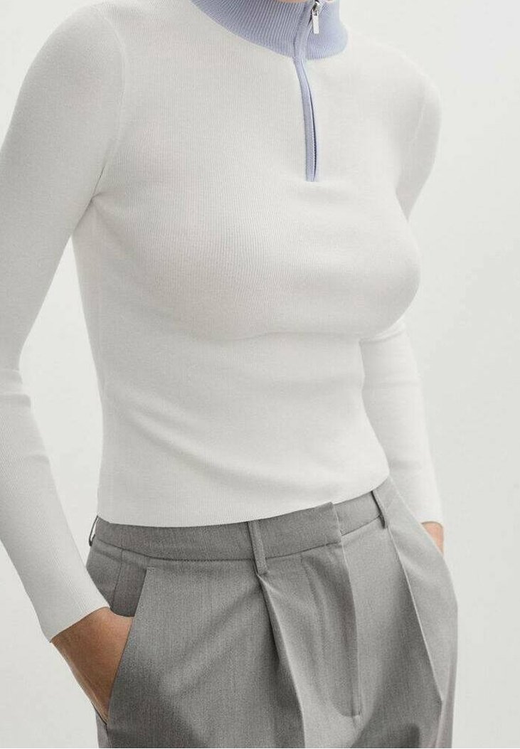 Fitted, weißes Rippoberteil mit langem Arm und einem lavendelfarbenen Reißverschlusskragen. Kombiniert mit grauen, gefältelten Hosen, die ein maßgeschneidertes Design präsentieren.