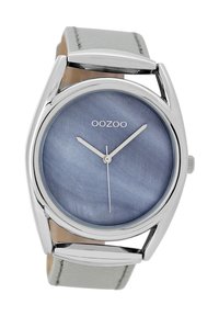 Montre argentée avec un cadran rond en marbre bleu, aiguilles des heures et des minutes en argent, et un bracelet en cuir gris avec des accents métalliques.