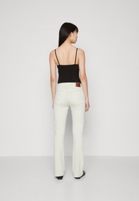 Jean évasés blancs avec une texture lisse, complétés par un haut à bretelles spaghetti noir. Présente une patte en cuir à l'arrière de la taille.