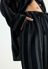 Set di camicia e pantaloni a strisce nere, realizzato in tessuto leggero. Caratterizzato da una vestibilità comoda, chiusure con bottoni e tasche laterali. Strisce bianche orizzontali.