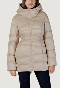 Giacca imbottita beige con cappuccio, dotata di chiusura a zip, vita arricciata e tessuto liscio. Il design include sezioni cucite orizzontali.