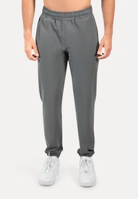 Grå træningsbukser med elastisk talje, tætsiddende pasform og elastiske manchetter ved anklerne, kombineret med hvide sneakers.