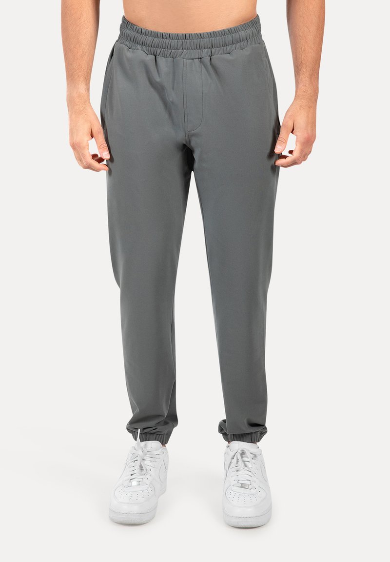 Grå træningsbukser med elastisk talje, tætsiddende pasform og elastiske manchetter ved anklerne, kombineret med hvide sneakers.