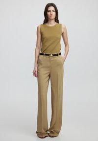 Top sin mangas de color verde oliva combinado con pantalones de pierna ancha beige de cintura alta, cinturón negro con hebilla circular dorada, textura de tela suave.