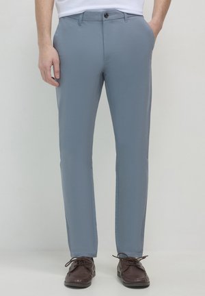 Pantaloni azzurri chiari con una vestibilità slim, realizzati in tessuto liscio. Presentano una chiusura con bottone frontale e tasche laterali. Abbinati a scarpe marroni.