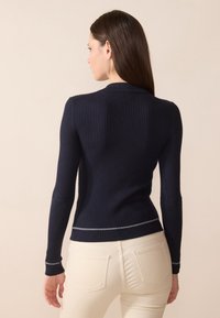 Pull en maille côtelée bleu marine, à manches longues, design ajusté et couture argentée au niveau de l'ourlet. Texture lisse, col plat et silhouette distincte.