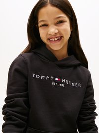 Melna kapuce ar priekšējo kabatu, ar baltu un sarkanu "TOMMY HILFIGER EST. 1985" tekstu. Mīksts audums ar brīvu piegriezumu un kapuci ar saiti.
