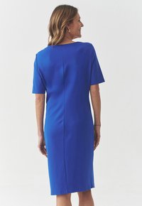 Blaues, tailliertes Kleid mit kurzen Ärmeln, glattem Stoff und knielanger Länge, das ein rückseitiges Nahtdetail aufweist. Einfaches, elegantes Design mit klaren Linien.