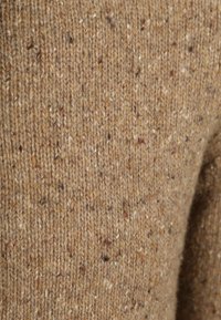 Bruin wollen stof met een gestructureerd, gebreid patroon, voorzien van vlekjes van lichtere en donkerdere vezels. Zachte en warme uitstraling.