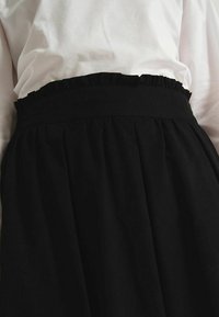 Jupe plissée noire avec une taille froncée, fabriquée dans un tissu doux. La ceinture est lisse, créant une silhouette raffinée.