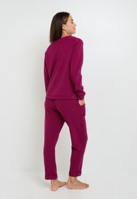 Ensemble de lounge magenta en tissu texturé ; comprend un haut à col rond à manches longues et un pantalon à poignets avec poches latérales.