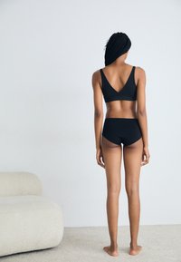 Black wireless bra with a V-back design and matching high-waisted briefs, crafted from soft fabric, shown from the back.