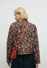 Jakke med leopardprint, lange ærmer, krave og cropped design. Komplementeret af en lille rød skuldertaske.
