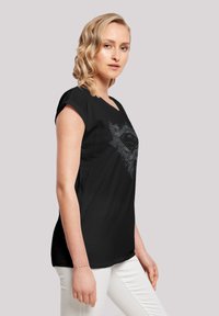 Black t-shirt with short rolled sleeves, featuring a gray graphic design of a shield with wings and a logo at the center.