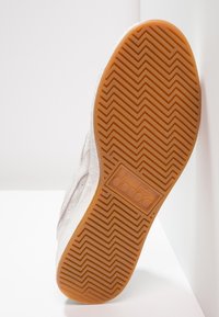 Podeszwa tenisówki wykonana z gumowej, teksturowanej gumy o wzorze jodełki, biały wierzch z delikatnym przeszyciem i detalem logo.