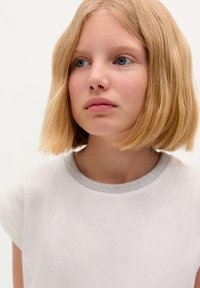 White t-shirt with a silver, textured collar. The design features short sleeves. Hair is straight and shoulder-length.