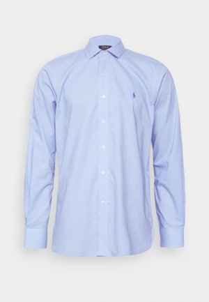 Hele sinine ruudulise mustriga pikkade varrukatega särk terava kaelusega, esipaneeli nööbid ja väike logo vasakul rinnal. Puuvillane kangas, sile tekstuur.