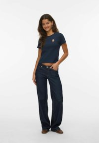 Mørkeblå T-shirt med korte ærmer og en bjørn-patch, parret med løstsiddende, mørke denim jeans med skræddersyet talje og lige ben.