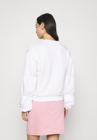 Sweatshirt branco com mangas bufantes, decote redondo e bainha canelada, combinado com uma saia de ganga rosa. Textura de tecido suave.