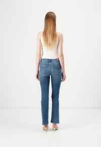 Blauwe denim jeans met een recht model, voorzien van achterzakken en een gemiddelde taille, gedragen met een aansluitend wit tanktop.