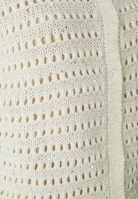 Megztinis off-white spalvos, su atvirojo mezgimo dizainu ir nėriniuota tekstūra. Papuoštas išsklaidytomis blizgučiais subtiliam žvilgesiui. Baigtas su ribotu kraštu.