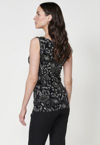 Haut sans manches noir avec des motifs floraux et géométriques complexes en blanc et gris. Design ajusté, texture lisse et décolleté rond.