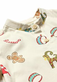 Cămașă de culoare crem, cu guler mandarin, închidere cu buton și imprimeuri tematice de sărbători, inclusiv bastonașe de zahăr și prăjiturele de turtă dulce.