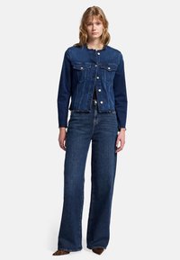 Dunkelblaue Jeansjacke mit zwei Fronttaschen, gerade geschnittenen Ärmeln und fransigem Saum, kombiniert mit weit geschnittenen dunkelblauen Jeans.