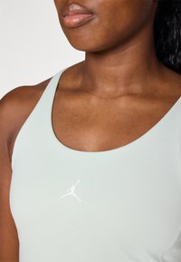 Sujetador deportivo verde claro con escote en forma de u y un logo de Jordan en blanco en el centro. Tela suave y elástica sin patrones ni elementos metálicos.
