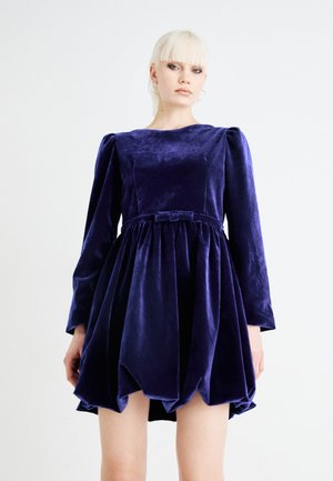 Purple velvet dress with long sleeves, round neckline, gathered skirt, and a bow at the waist. Smooth texture, knee-length hem.