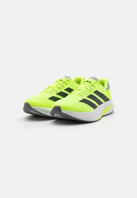 Bright neon yellow athletic shoes with black stripes, gray accents, textured mesh upper, and a white sole featuring a flexible design.