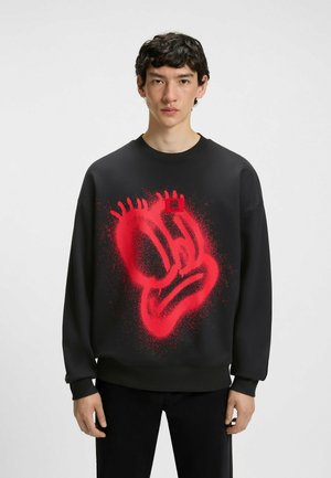 Sudadera negra con un gran gráfico de cara en estilo spray rojo. Presenta un cuello redondeado y puños acanalados. Etiqueta de la marca visible.