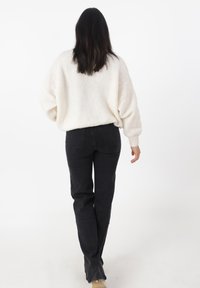 Witte, oversized trui met gestructureerd breiwerk, gecombineerd met zwarte rechte jeans. De outfit heeft een relaxte pasvorm en een eenvoudig ontwerp.