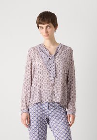 Pitkähiha blouse vaaleanliilassa, jossa on toistuva geometrinen kuvio; frilla kauluksessa; yhdistetty vastaavasti kuviollisiin housuihin.