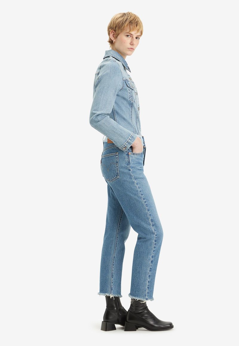 Lichtblauwe denimjacket met een traditionele kraag, borstzakken en lange mouwen, gecombineerd met lichtblauwe cropped jeans en zwarte enkellaarzen.