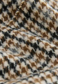 Wool fabric with a houndstooth pattern in beige, brown, and black tones. Soft texture with visible fibers and stitching details.