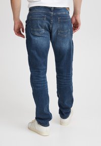 Blå denimjeans med smal passform, fem lommer og subtil falming. Har kontrasterende oransje sømmer og en lærflekk på baksiden.