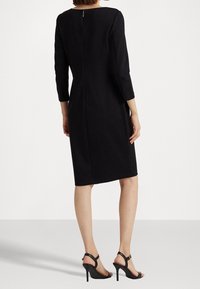 Svart klänning i knälängd med trekvartsärmar, figursydd design, mittbakdragkedja, slät textur, kombinerad med svarta högklackade sandaler.