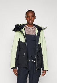 Giacca GORE-TEX con un design a blocchi di colore verde chiaro e nero, tasche con zip e cappuccio. Tessuto testurizzato con accenti a contrasto.