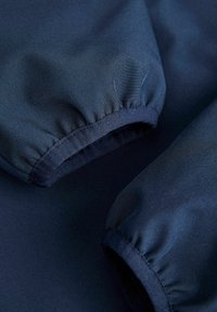 Σκούρο μπλε υφασμάτινα μανίκια με ελαστικά μανσέτες, που δείχνουν κοντινή υφή και λεπτομέρειες ραφής.