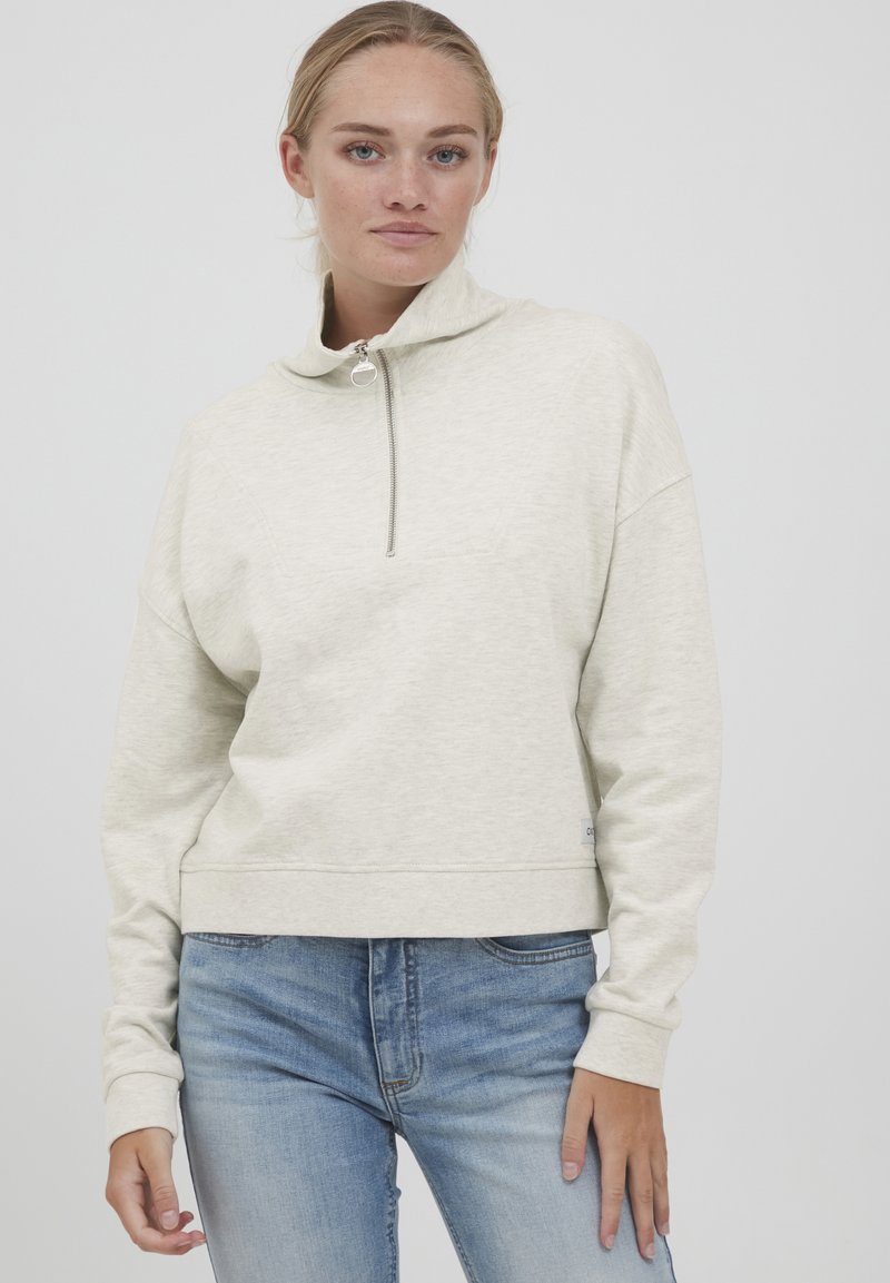 Lys beige cropped sweatshirt med høj krave og halv lynlås. Blødt stof, langeærmer, ribbede manchetter og en subtil tekstur.