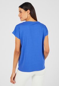 T-shirt blu a maniche corte realizzato in tessuto morbido; presenta una vestibilità comoda con scollatura rotonda e orlo dritto, indossato con pantaloni bianchi.