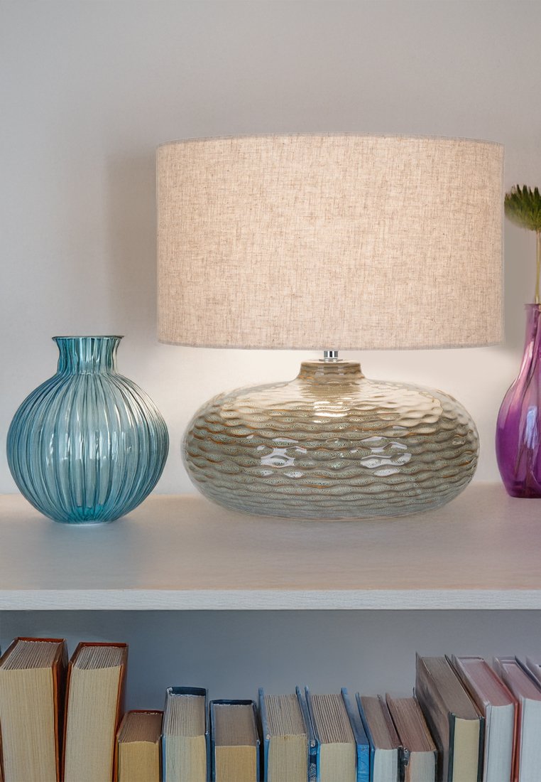 Keramiklampe mit gewelltem, strukturiertem Sockel in Hellbeige, gekrönt mit einem beigen Stoffschirm; begleitet von einer blauen gerippten Glasvase.