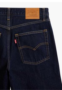 Vaqueros de mezclilla índigo con un parche de cuero con marca, costuras doradas y dos bolsillos traseros que cuentan con el diseño emblemático característico de Levi's.