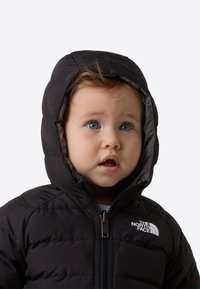 Czarna kurtka puchowa z kapturem, zamkiem błyskawicznym i białym logo. Materiał wydaje się gładki z pikowanym wzorem.