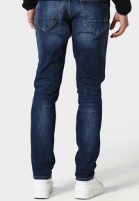 Plonos silueto džinsai tamsiai mėlyno džinso audinio su švelnia tekstūra, penkių kišenių dizainu ir dekoratyvinėmis siūlėmis ant nugarinių kišenių.