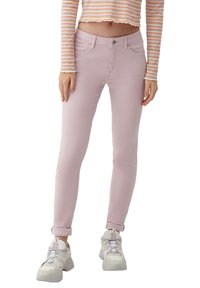 Femme portant un pantalon slim rose clair, des baskets blanches épaisses et un haut rayé court à manches longues.